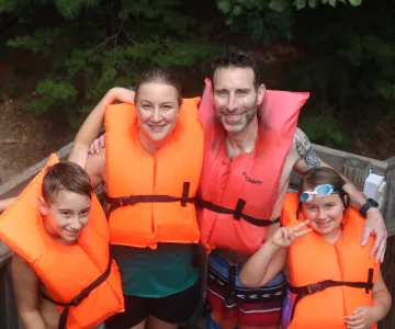 Family of four hugging each others shoulders while wearing PFD's lined up to do the lake slide.