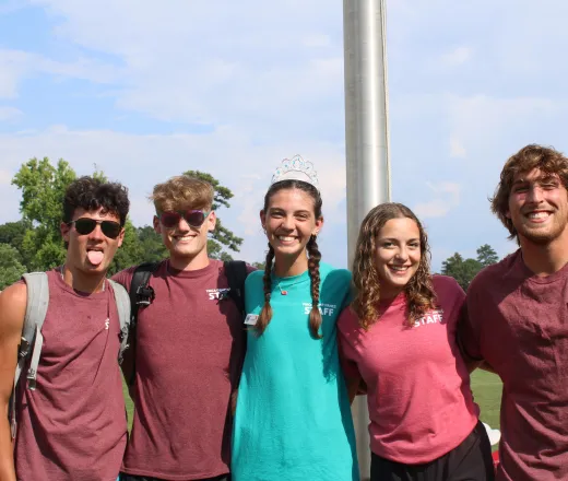 Five staff with their arms over each others shoulders smiling.